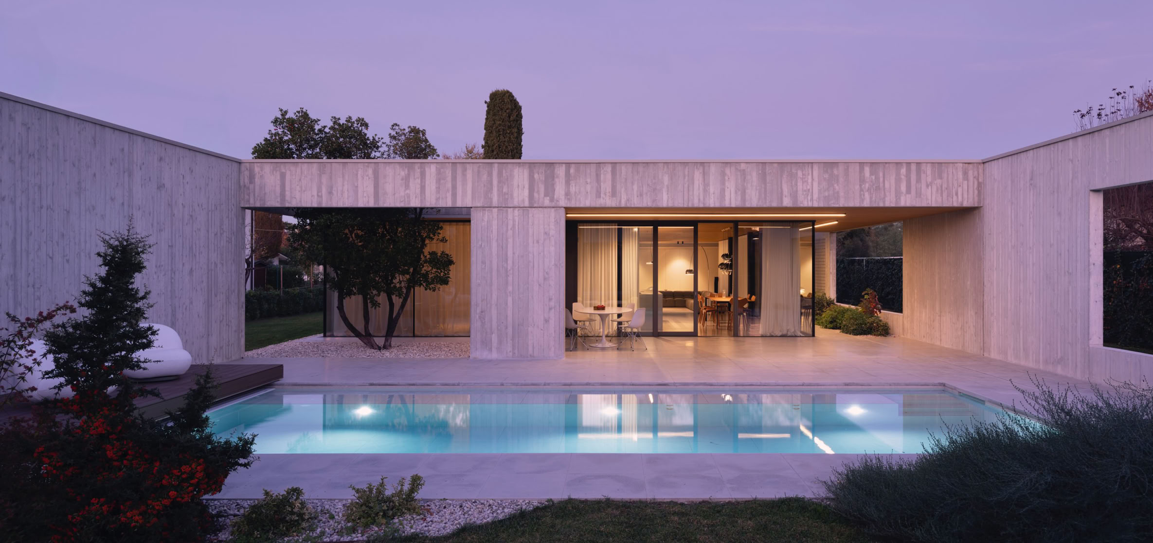 Contemporary single-level villa by MIDE architetti on the Piave River, combining privacy, open-space living, large glass windows, natural materials, and seamless integration with the surrounding landscape. Contemporary single-family house designed by MIDE architetti, blending exposed concrete and natural wood. Open-plan living, central patio, and seamless connection with nature and garden.