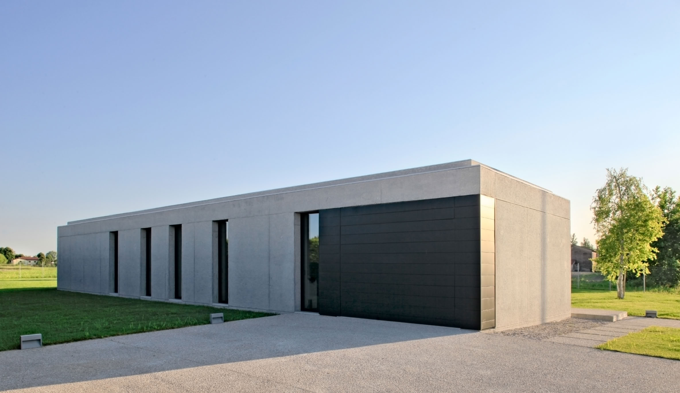 Single-story villa designed by MIDE architetti, featuring essential sandblasted concrete volumes and large glass walls facing the garden.
