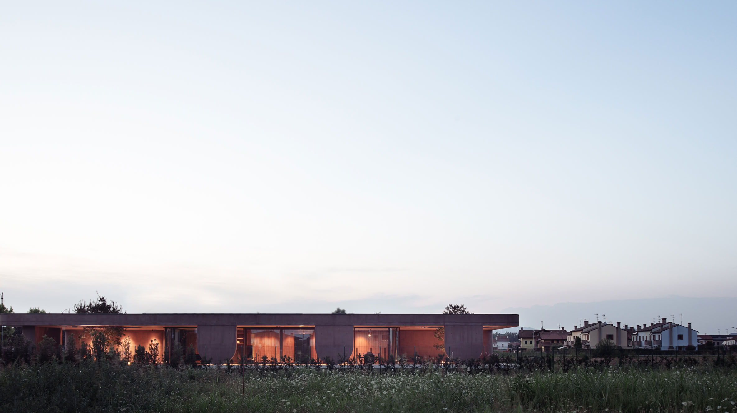 Vista dell'ampio portico con pilastri materici e aperture con vegetazione inserita. 