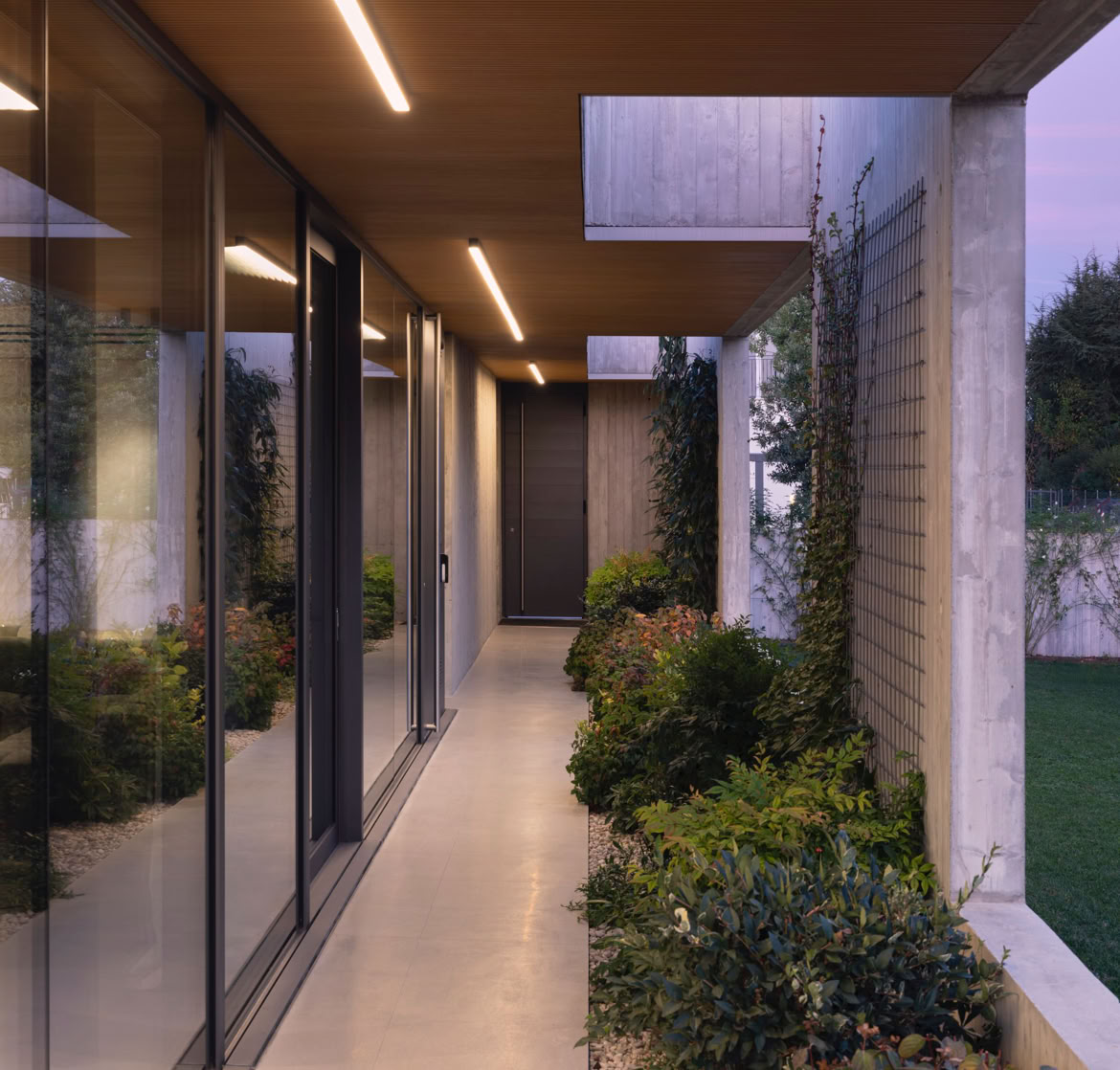 View of the outdoor portico of the Piave Villa, designed by MIDE architetti, surrounded by greenery and defined by clean geometric forms that enhance privacy and create a sheltered living environment.