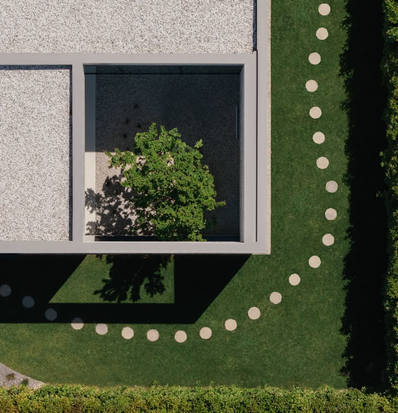 Central courtyard of the villa designed by MIDE Architetti, where exposed concrete interacts with vegetation, creating a suspended atmosphere between indoors and outdoors.