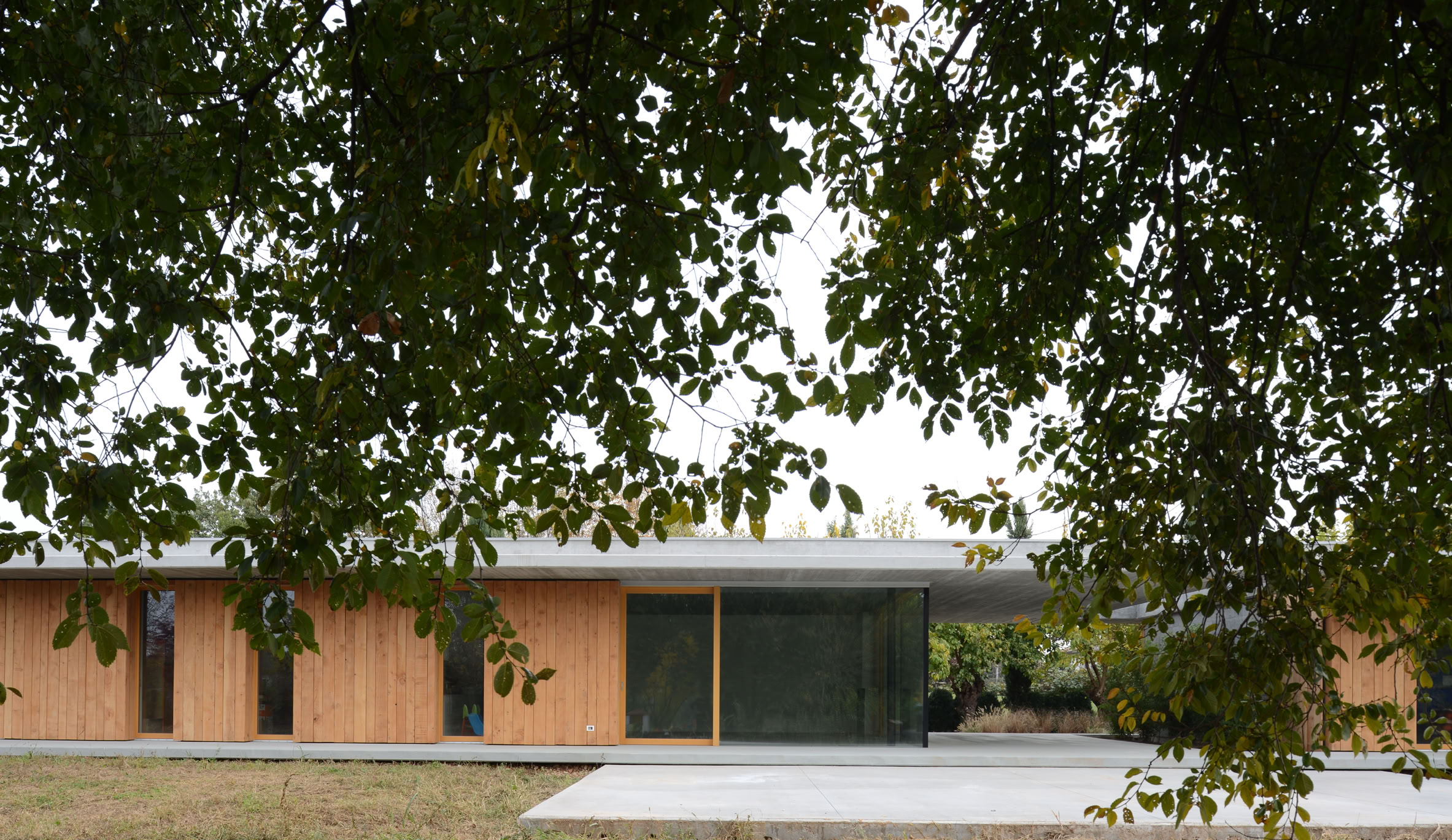 External view of the single-family villa in Montebelluna, Treviso, surrounded by greenery, featuring clean horizontal lines and large windows.