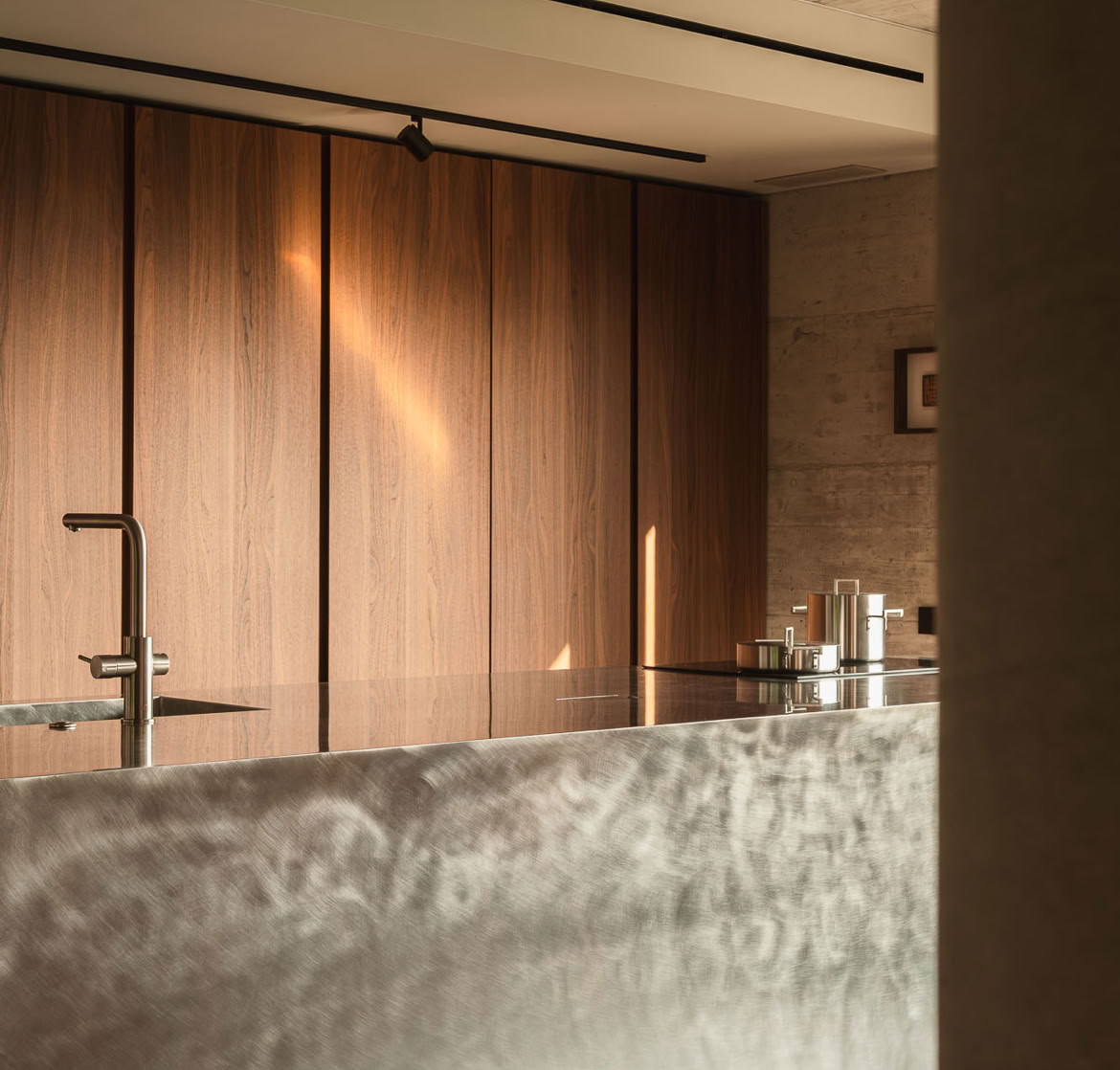 Vista della cucina contemporanea con isola e bancone in acciaio. Armadiature su misura in legno caldo completano l'ambiente.