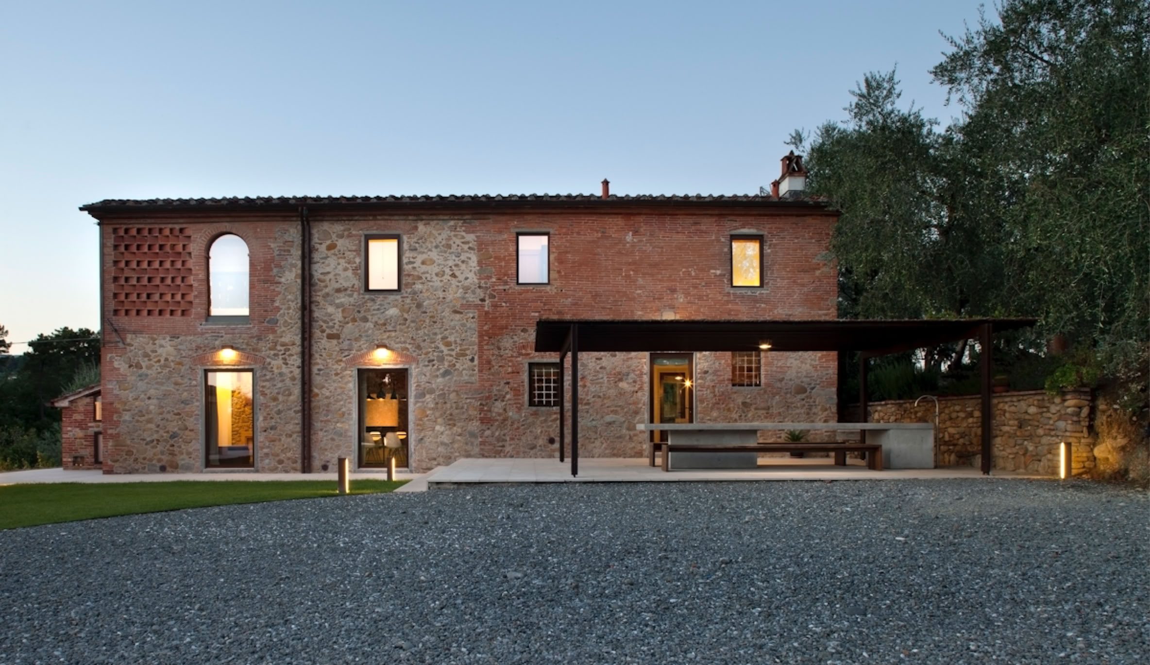 Facciata in pietra e mattone faccia a vista, con infissi in acciaio e scuri in legno che valorizzano l’architettura tradizionale toscana.