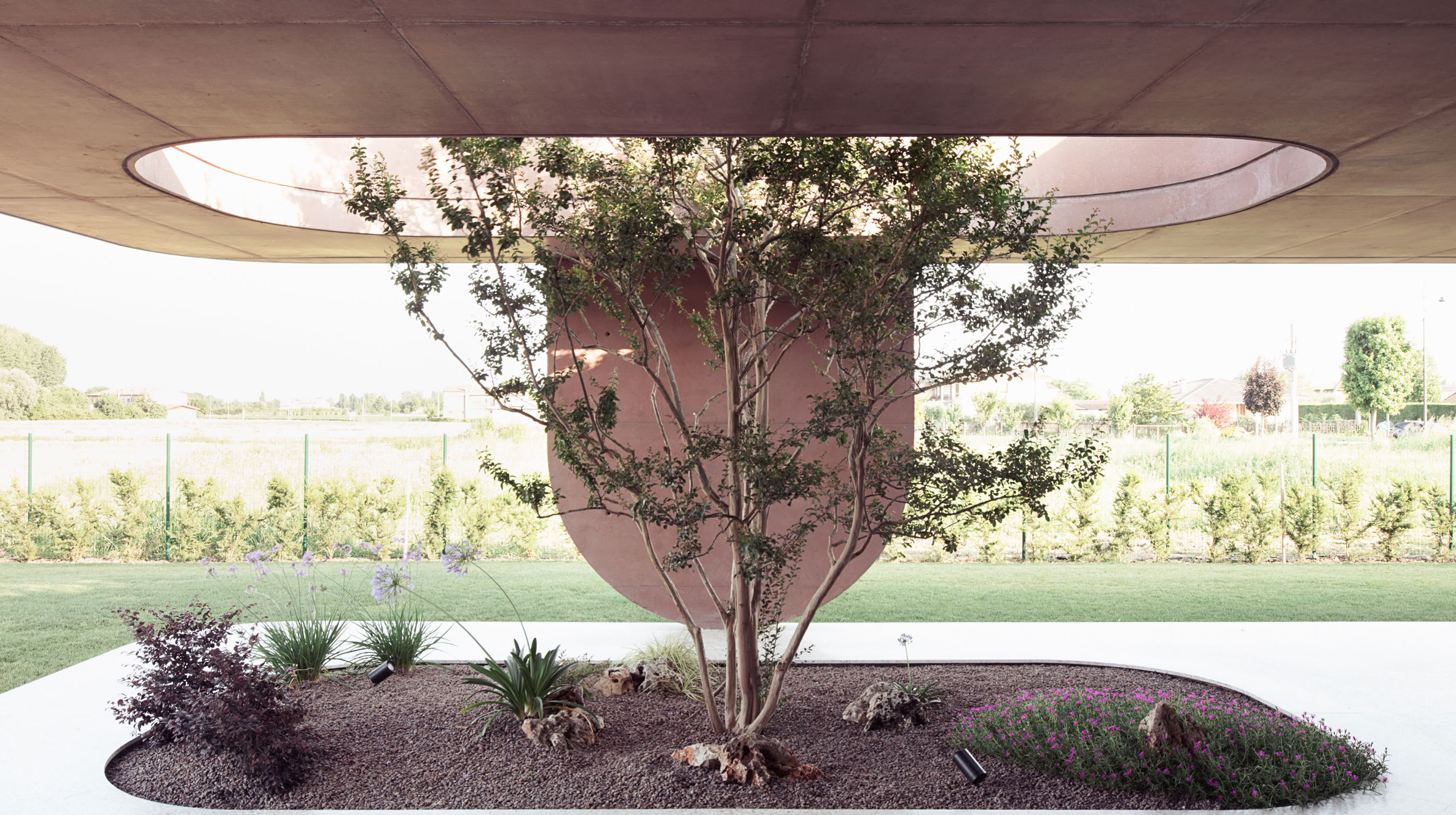 View of the wide portico with textured pillars and openings integrating vegetation.