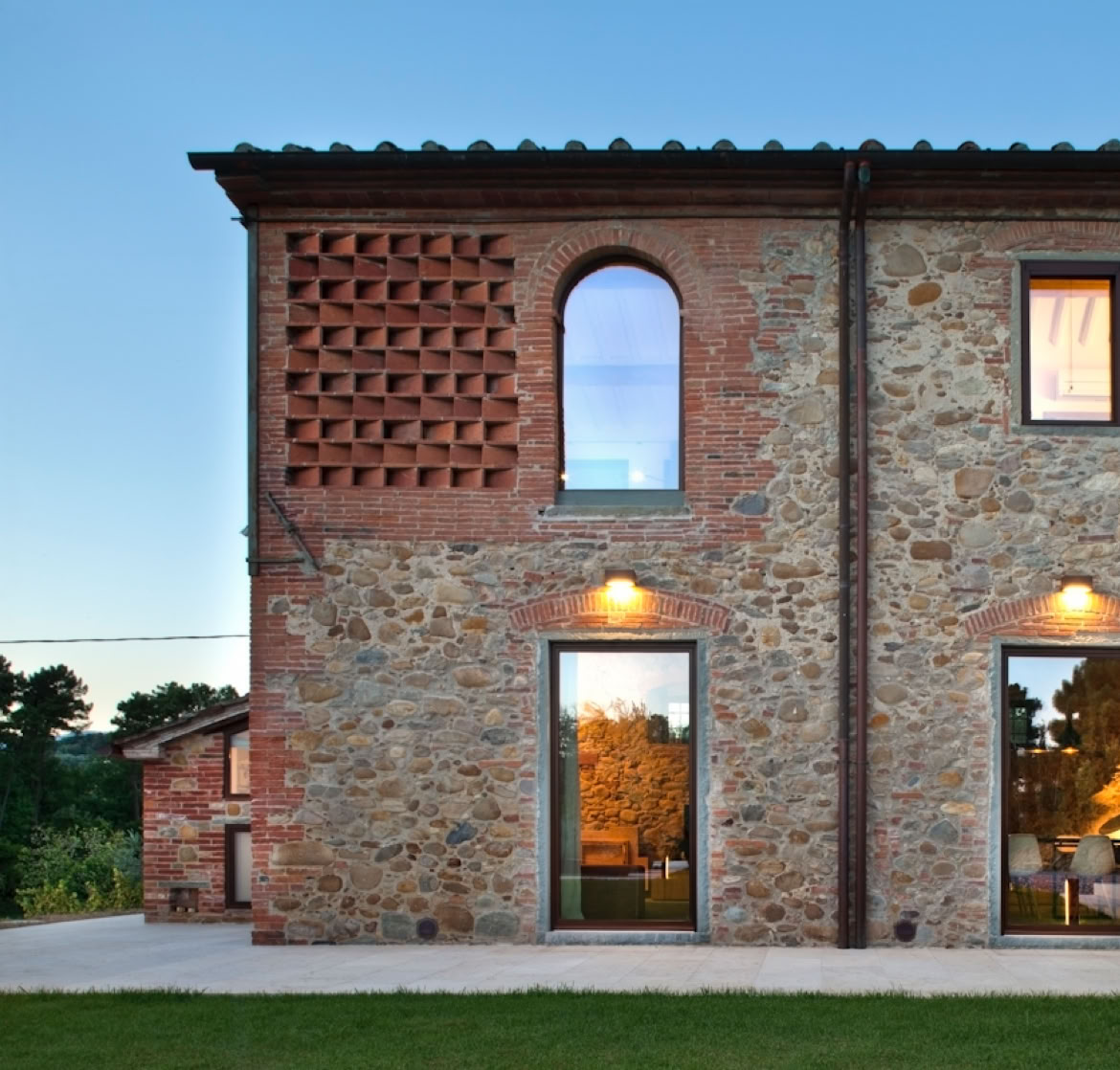 Stone and exposed brick façade of historic Tuscan farmhouse with steel frames and wooden shutters.