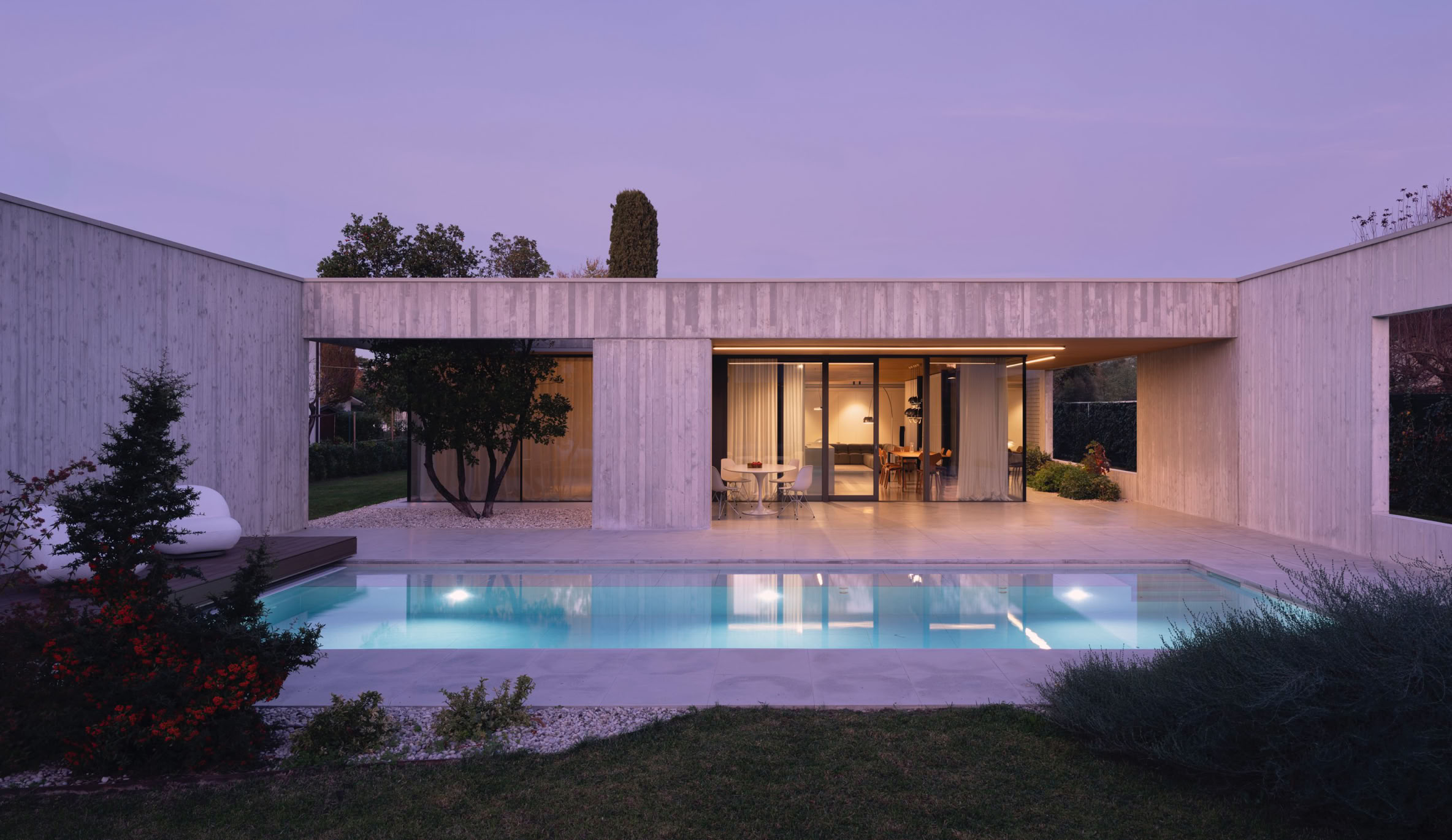 Vista serale sulla piscina outdoor della villa sul Piave realizzata da MIDE architetti. Un portale scenico inquadra il giardino permettendo allo stesso tempo di mantenere la privacy.