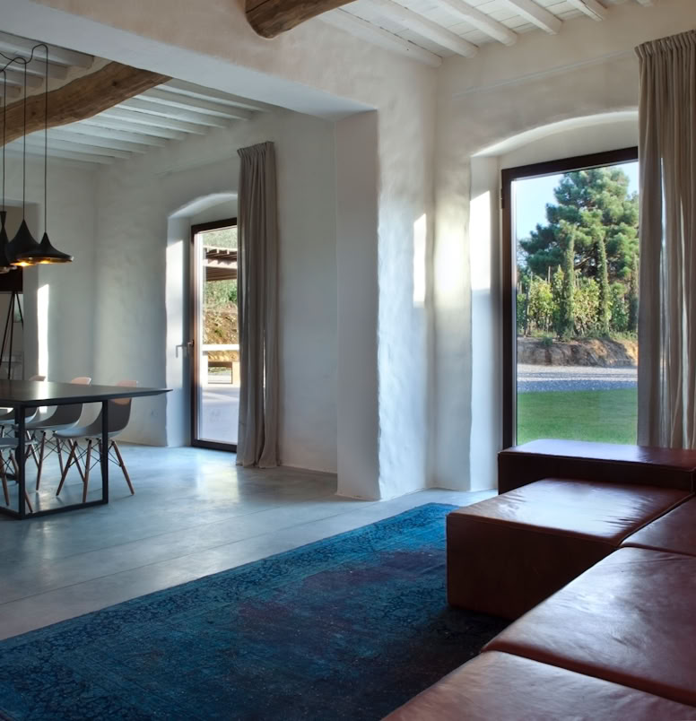Spacious living room with restored original beams and terracotta bricks, whitewashed ceilings, and natural light controlled by steel window frames.